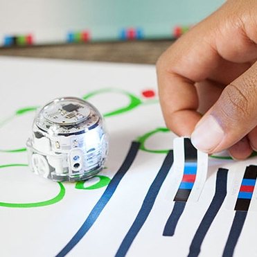 photo of an Ozobot mini robot with a young person's hand manipulating the pieces