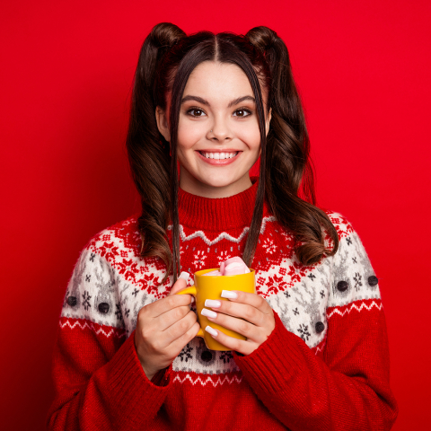 photo of a smiling teen girl with brown hair wearing a red and white holiday sweater holding a yellow mug against a red background