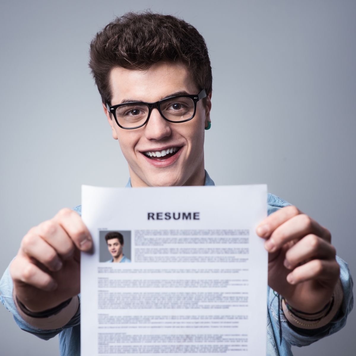 teenage boy with brown hair and glasses holding up his job resumé